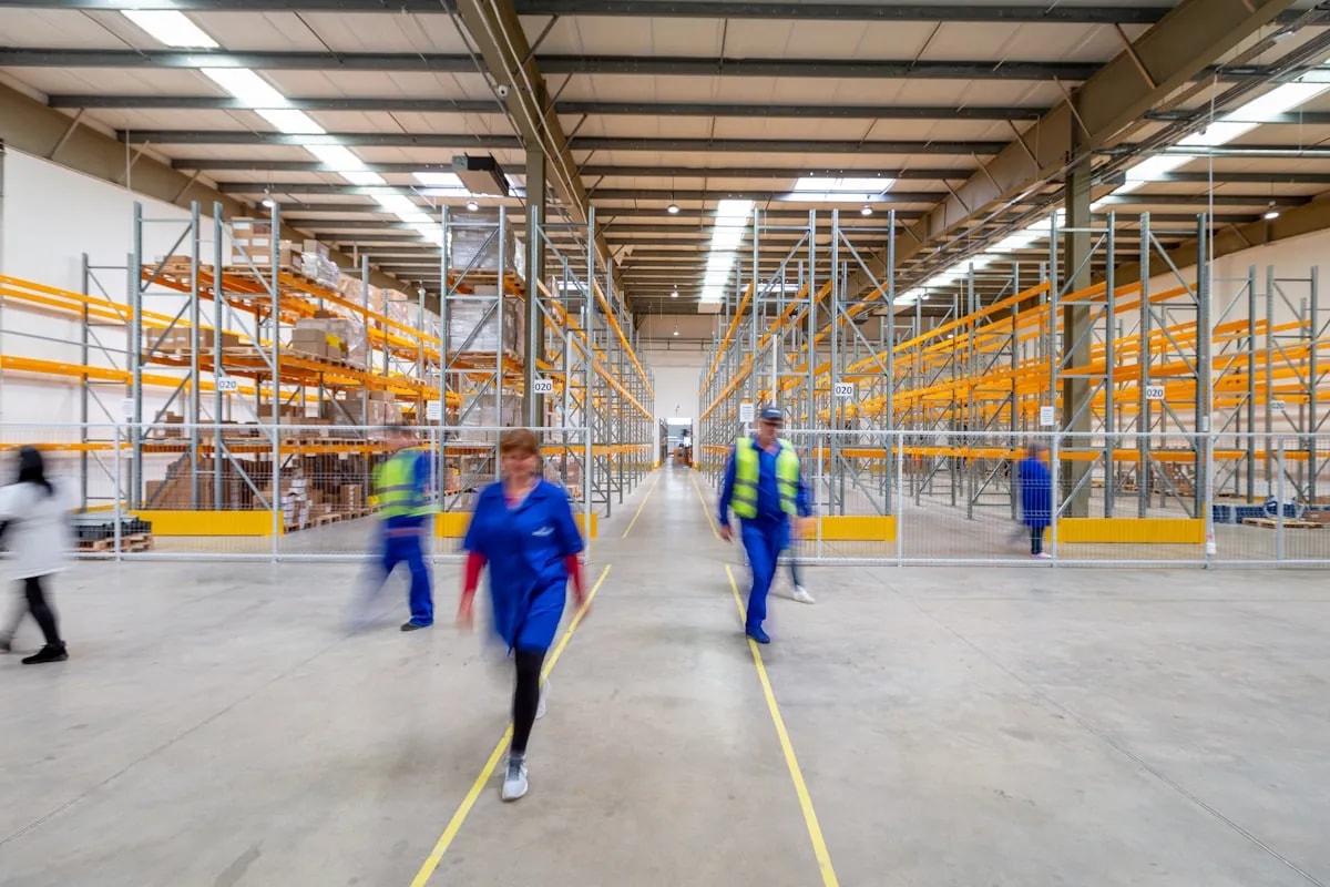 Workers walking through a warehouse aisle, illustrating vision-based attendance and safety monitoring for distributed teams